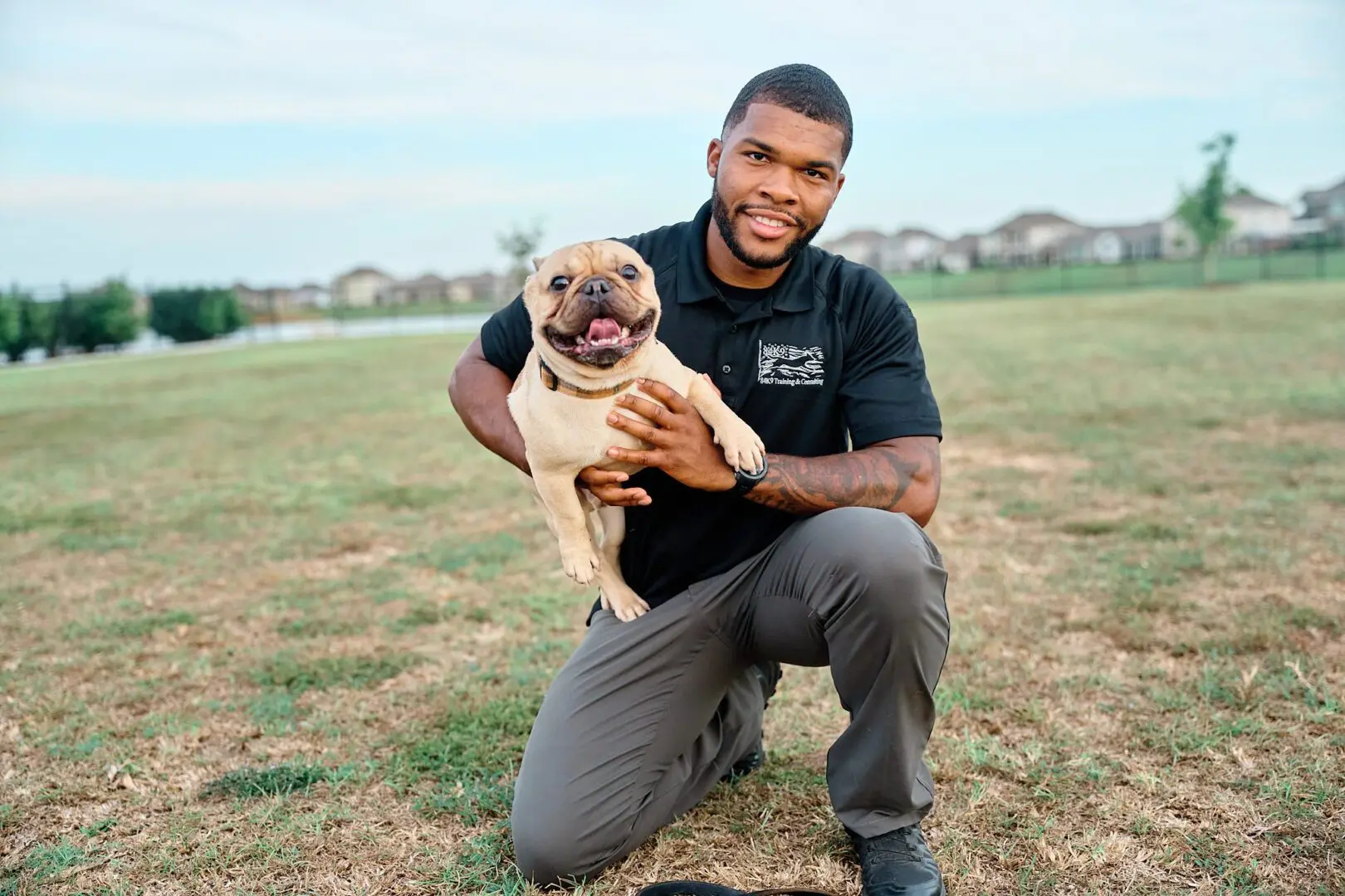 Man happily holding a small dog outdoors in a grassy area.