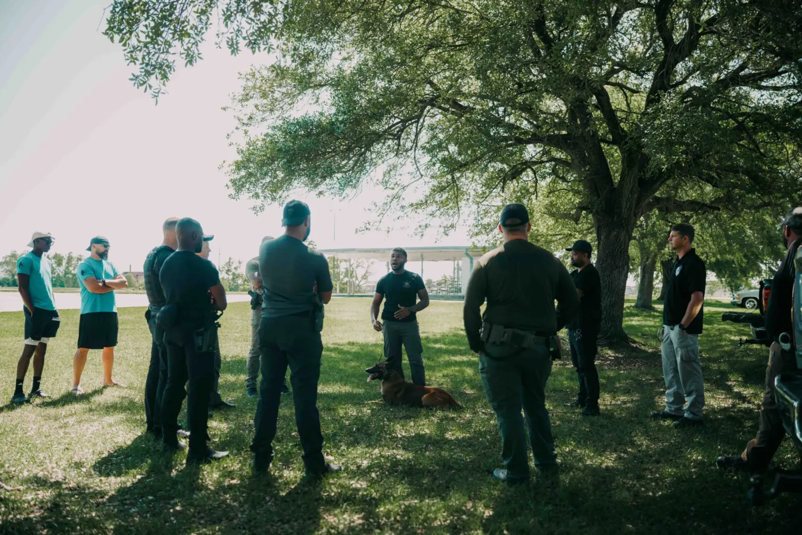 Police officers stand in a shaded park area near a body of water.