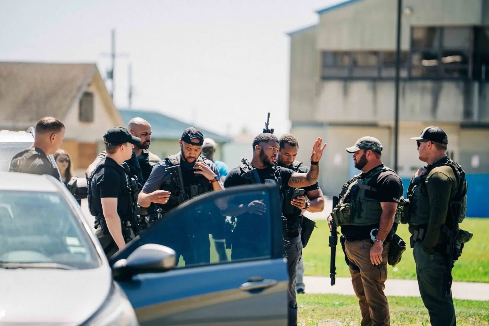 Police officers gather and communicate beside a vehicle outdoors.