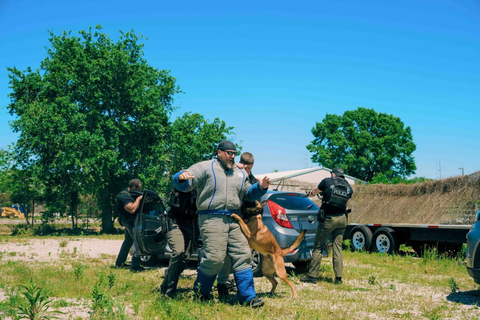 Military personnel in tactical gear preparing near a vehicle in a grassy area.
