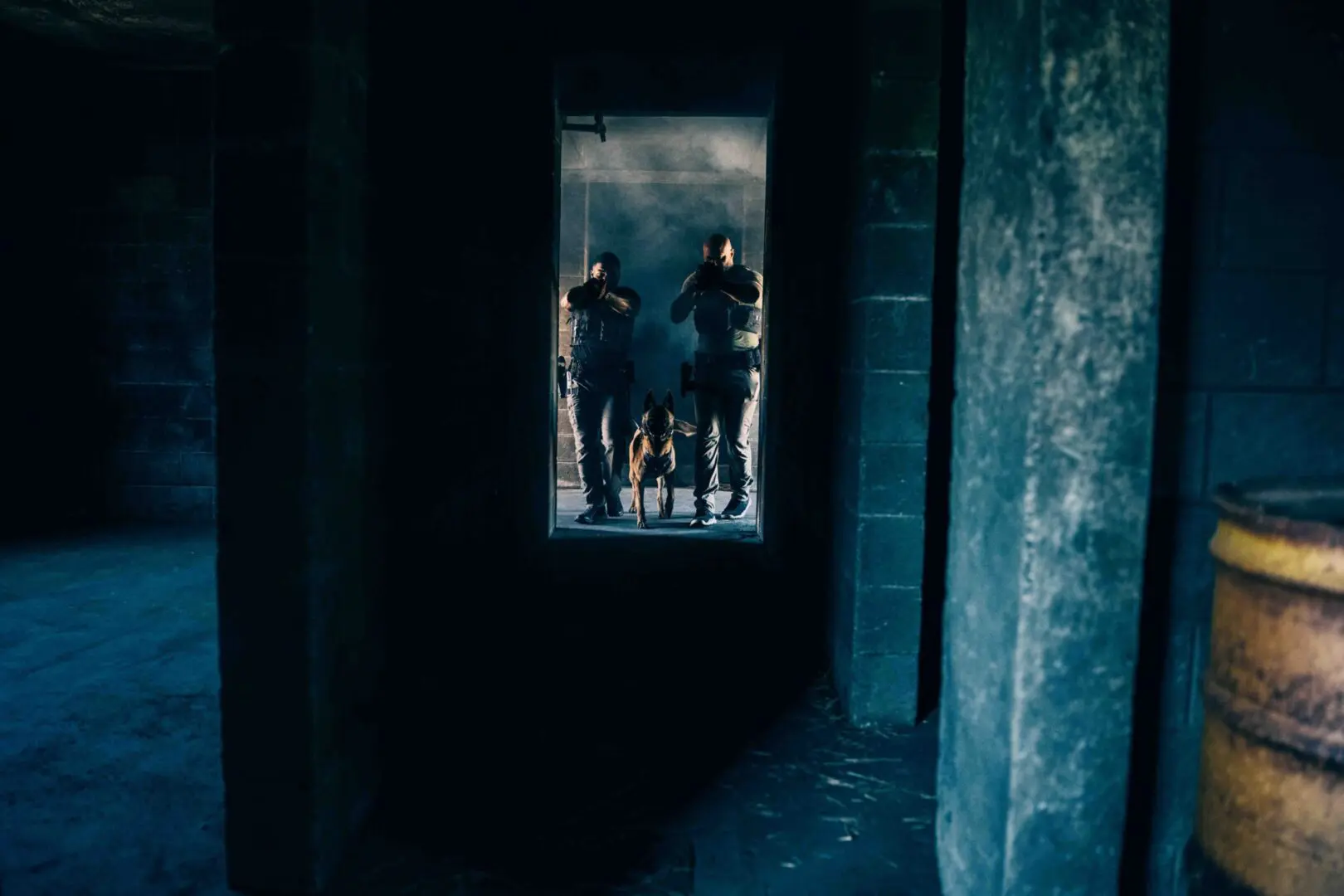 Two armed soldiers escort a kneeling prisoner down a dark corridor.