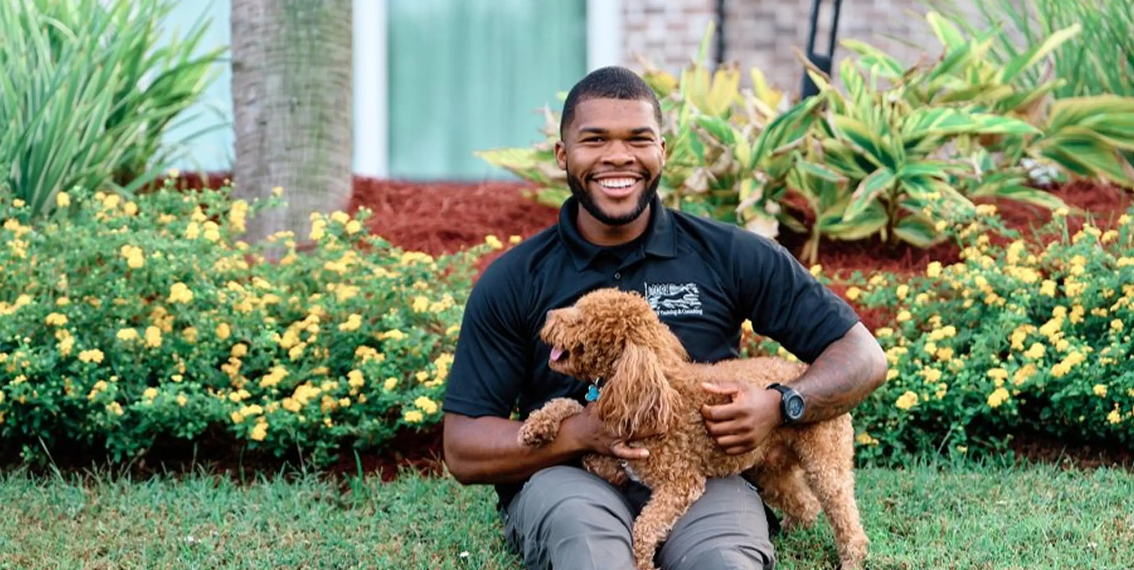 A smiling man sitting outdoors holding a small brown dog.
