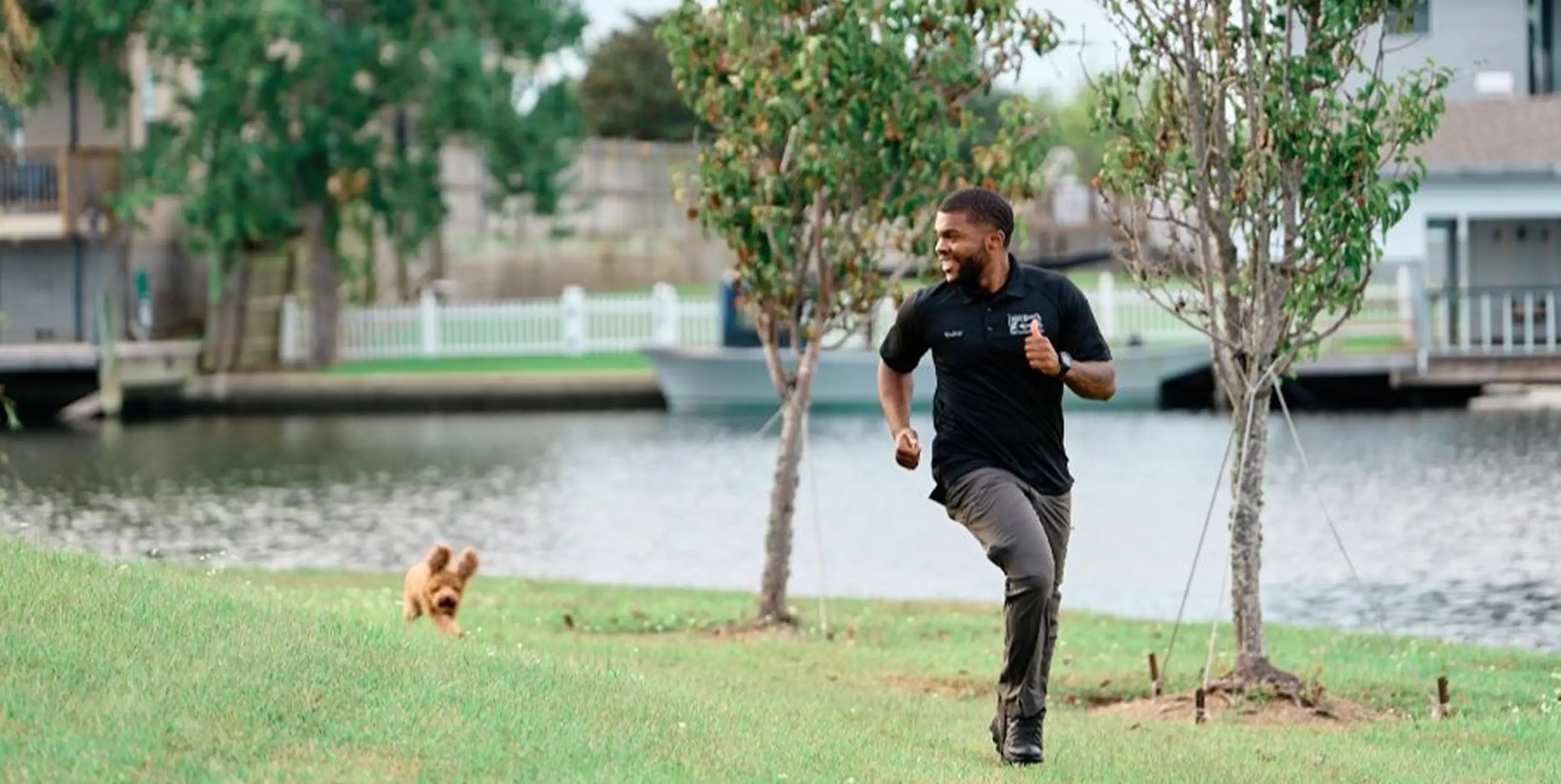 Man joyfully running with his small dog in a park near a lake.